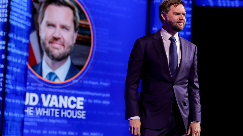 JD Vance on stage with picture in background