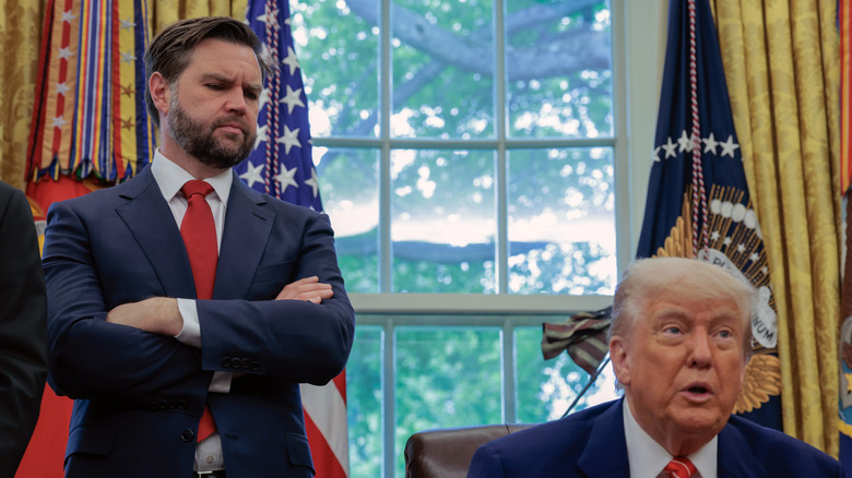 JD Vance standing with arms crossed behind Donald Trump