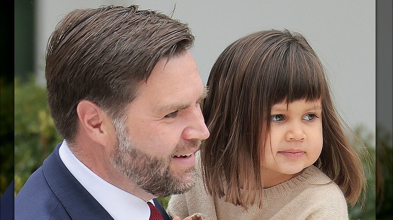 JD Vance holding Mirabel in a beige sweater with both looking to the right