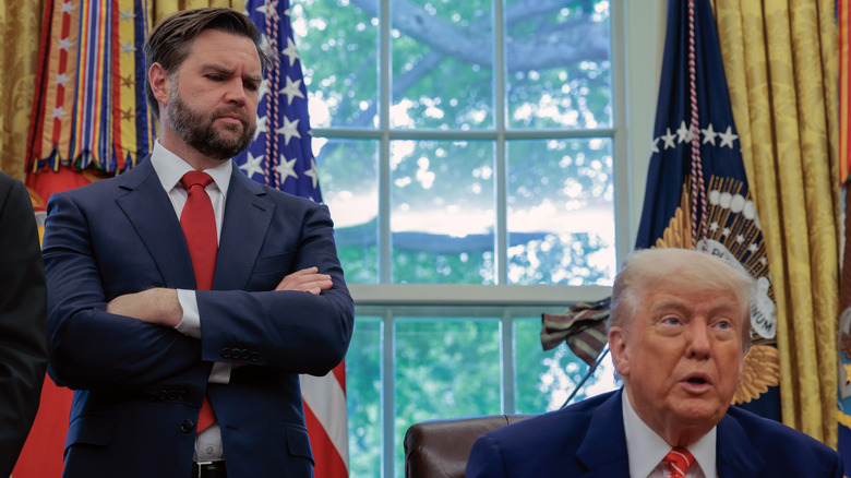 JD Vance crosses his arms and looks down at Donald Trump