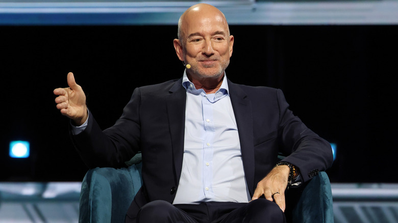 Jeff Bezos addressing an audience in a black suit with a light blue shirt underneath