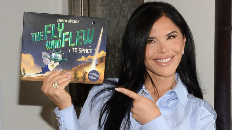 Lauren Sánchez Bezos smiling and pointing at a copy of 'The Fly Who Flew to Space'