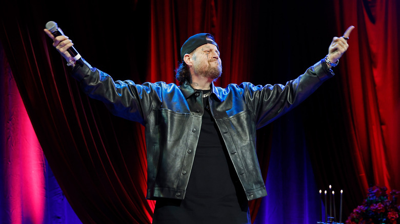 Jelly Roll stands with his arms outstretched and microphone in hand during a 