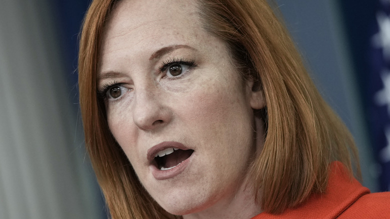 Jen Psaki wearing a red suit in the White House briefing room
