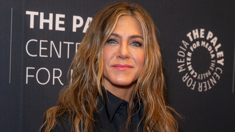 Jennifer Aniston smiling in front of black backdrop with white text