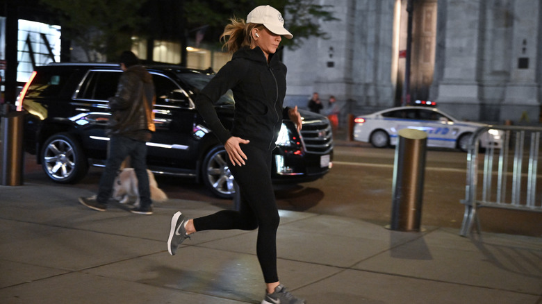 Jennifer Aniston jogging in black leggings and top and white ball cap