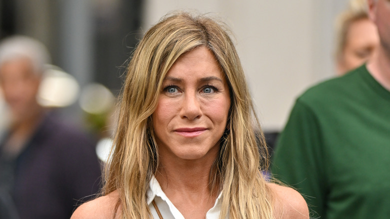 Jennifer Aniston smiling on 'The Morning Show' set while wearing a white dress.