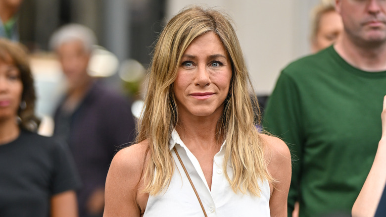 Jennifer Aniston walking outdoors with eye bags in a white collared top