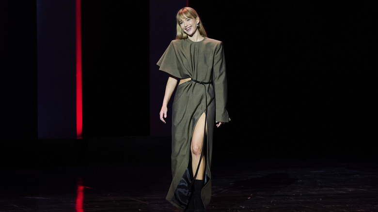 Jennifer Lawrence walking in an olive green dress with a slit and asymmetrical sleeves