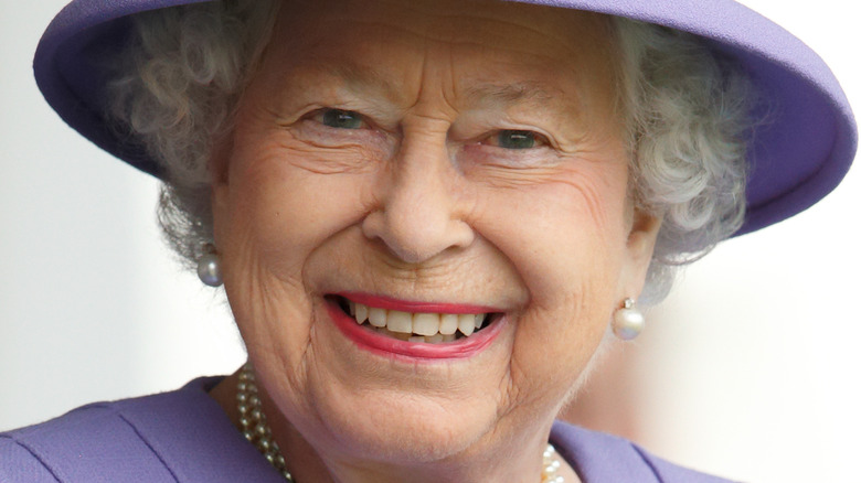 Queen Elizabeth smiling under a purple hat
