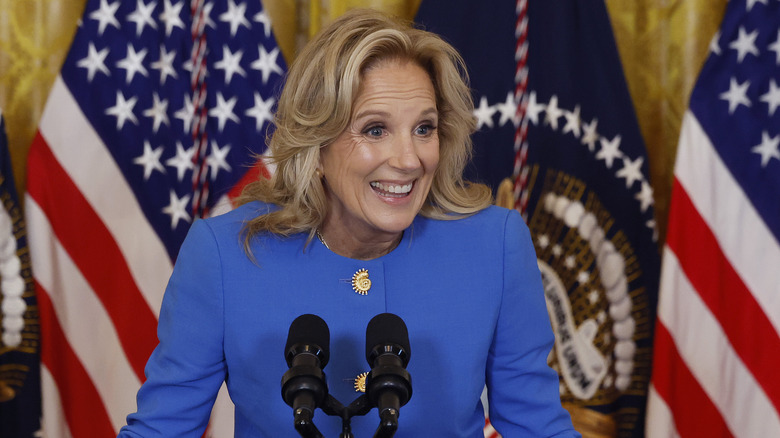 Jill Biden smiles at a podium with American flags in background