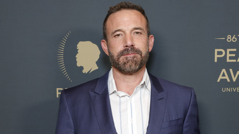 Ben Affleck posing on the red carpet in a dark blue suit and open-collared shirt