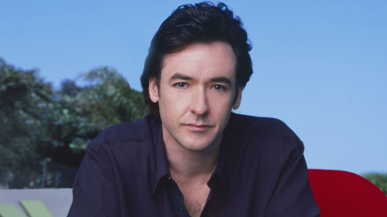 John Cusack poses for a photo in a room with blue background