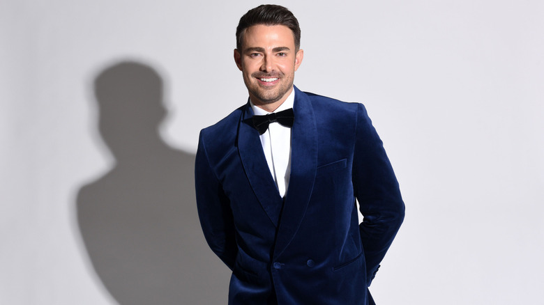 Jonathan Bennett smiling and posing wearing a blue velvet suit.