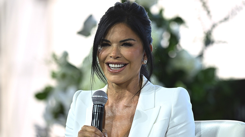 Lauren Sánchez Bezos smiling and holding a microphone in a white blazer