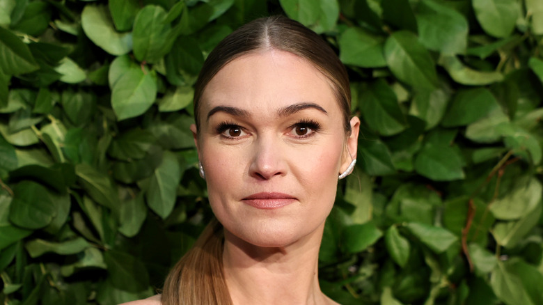 Close-up of Julia Stiles standing against a leafy green backdrop at the Gotham Awards.