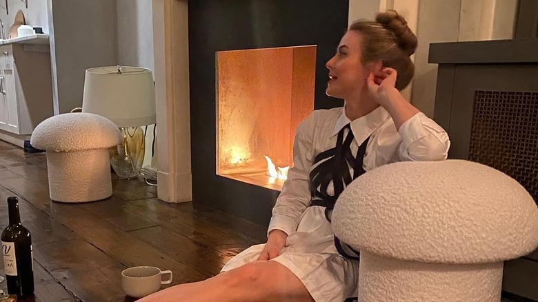 Julianne Hough sitting on the floor of her NYC apartment in a shirt dress with a bottle of wine and beside her