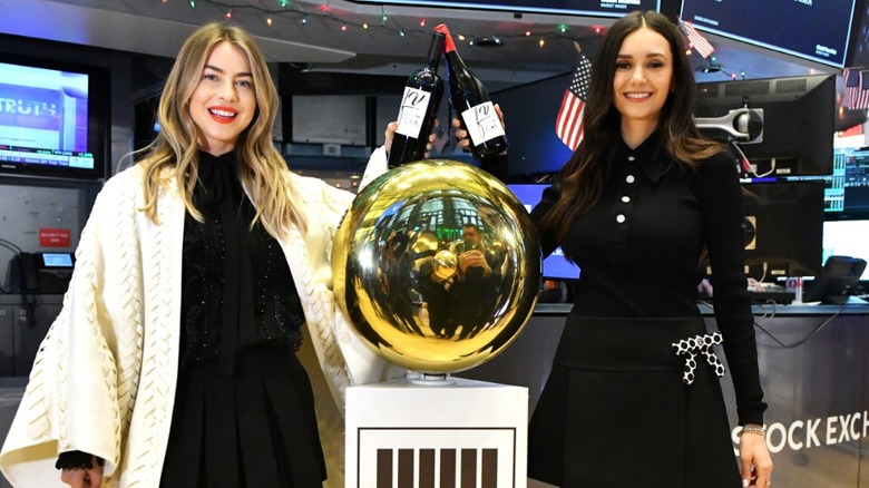 Julianne Hough and Nina Dobrev holding bottles of their wine on the floor of the New York Stock Exchange
