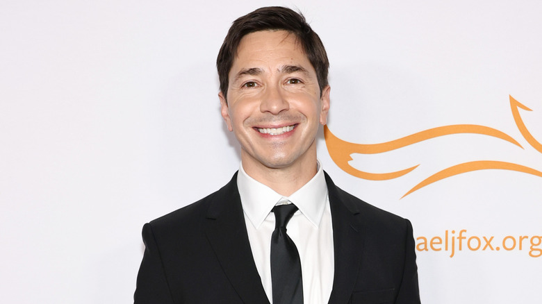 Justin Long smiling on the red carpet in a suit and tie