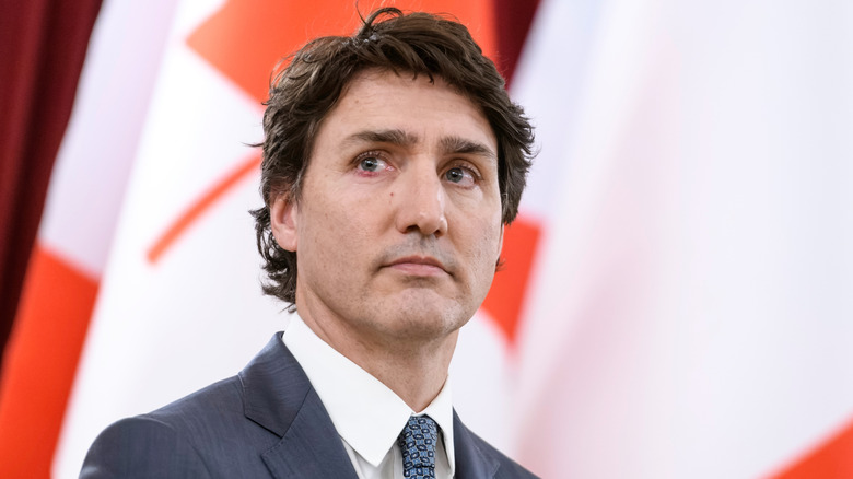 Justin Trudeau in a suit standing in front of Canadian flags.
