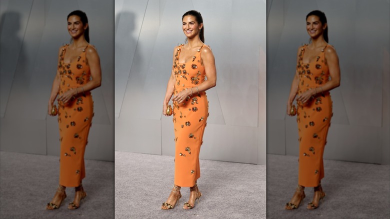 Kaitlan Collins smiling in an orange dress with gold floral details.