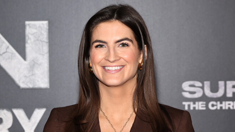Kaitlan Collins smiling while posing at an event in a brown blazer