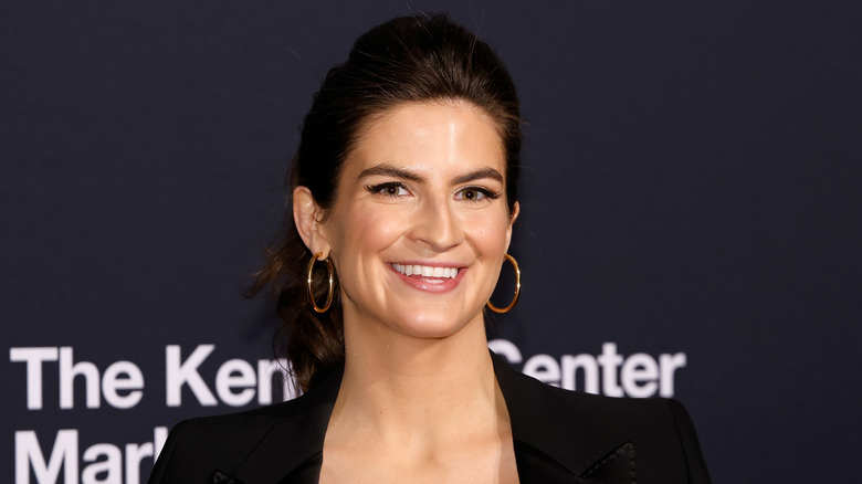 Kaitlan Collins smiling at the Mark Twain Prize red carpet wearing a black shirt and black blazer.