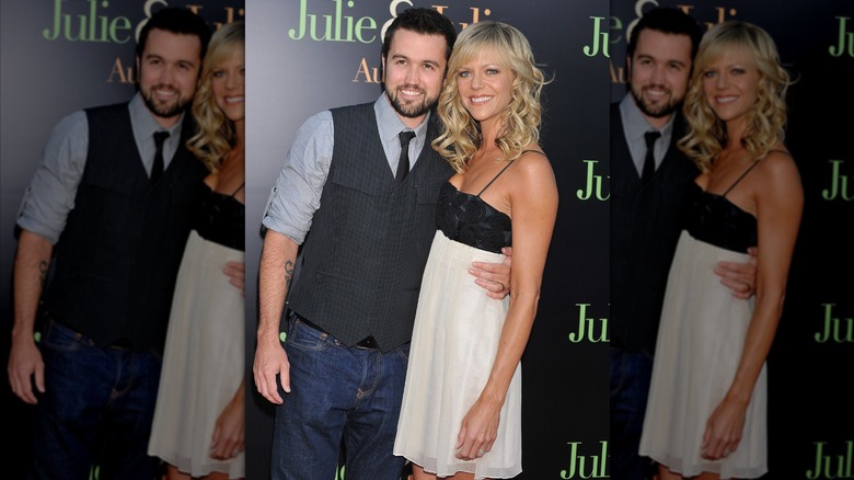 Rob McElhenney wearing a dark gray vest and light gray shirt and posing with his arm around Kaitlin Olson, who wears a black and white empire-waist dress.