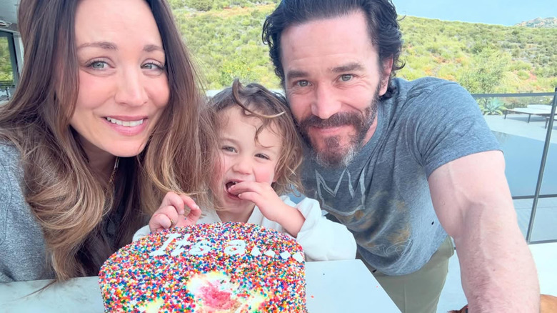 Kaley Cuoco, Tom Pelphrey, and their young daughter posing with a cake with colorful sprinkles.