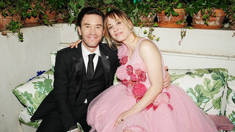 Tom Pelphrey and Kaley Cuoco smiling on a couch together.