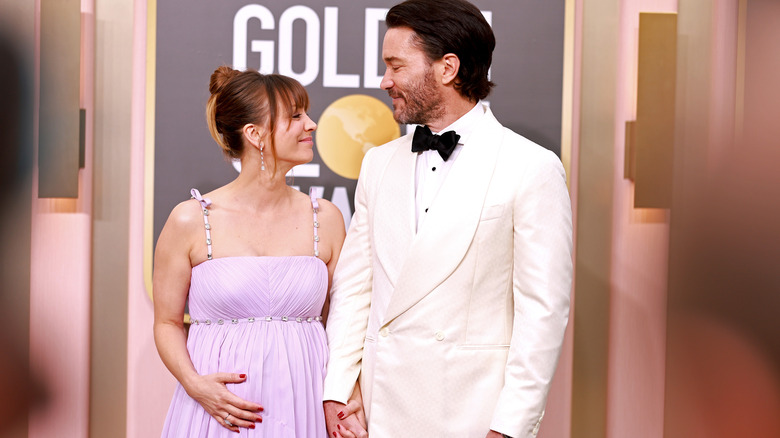 Pregnant Kaley Cuoco and Tom Pelphrey hand in hand and smiling at each other.