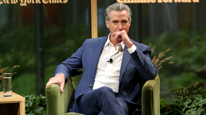 Gavin Newsom sitting at an event with his hand to his mouth in a dark blue suit