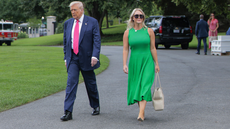 Karoline Leavitt walking next to Donald Trump in a green dress with a beige handbag