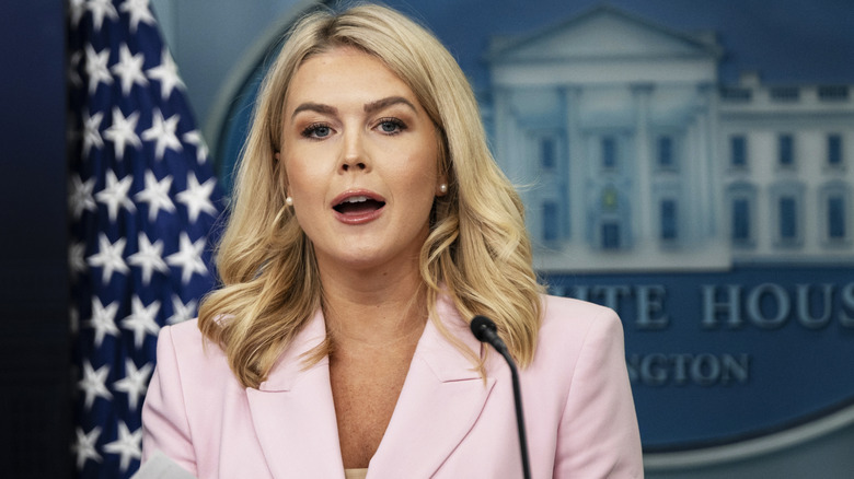 Karoline Leavitt mouth open in the White House press briefing room in a light pink blazer