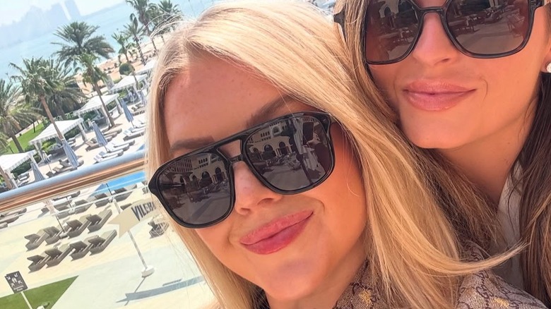 Karoline Leavitt, wearing sunglasses, posing with Margo Martin in front of a beach-like area.