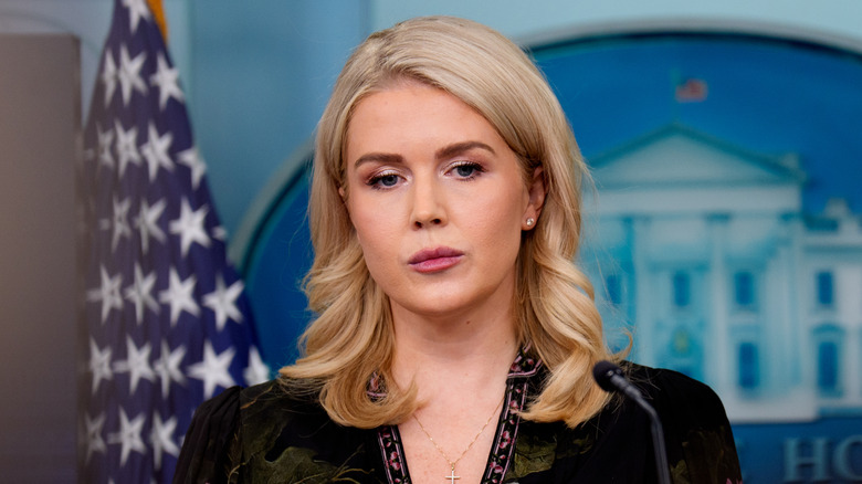 Karoline Leavitt in the White House Press Room, behind microphone in a black and green top.
