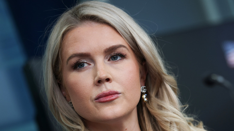 Close up of Karoline Leavitt behind a microphone with a plain expression and dangling earrings.