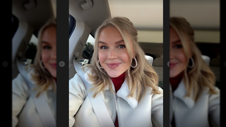 Karoline Leavitt smiling in a car, taking a selfie wearing a red turtleneck and hoop earrings.