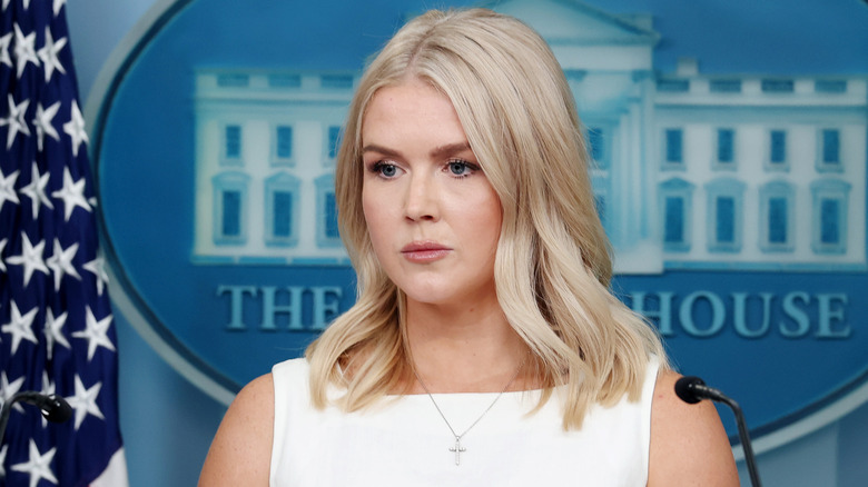 Karoline Leavitt looking concerned in a white strapless dress and a cross necklace