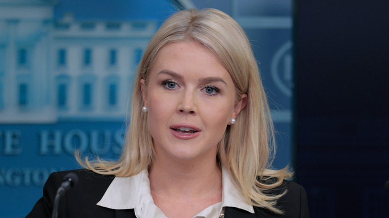 Karoline Leavitt speaking at a press conference while wearing a black blazer and white collared shirt.