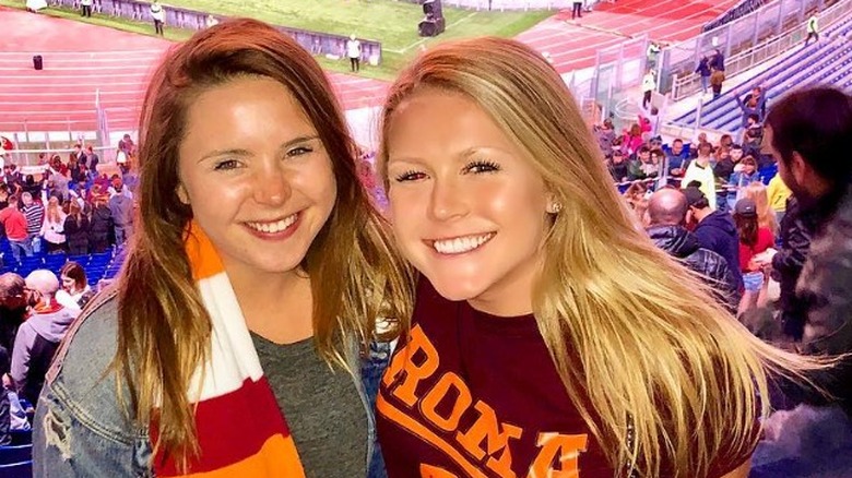 Karoline Leavitt smiling in a dark red shirt and a pair of blue jeans at a sports game.