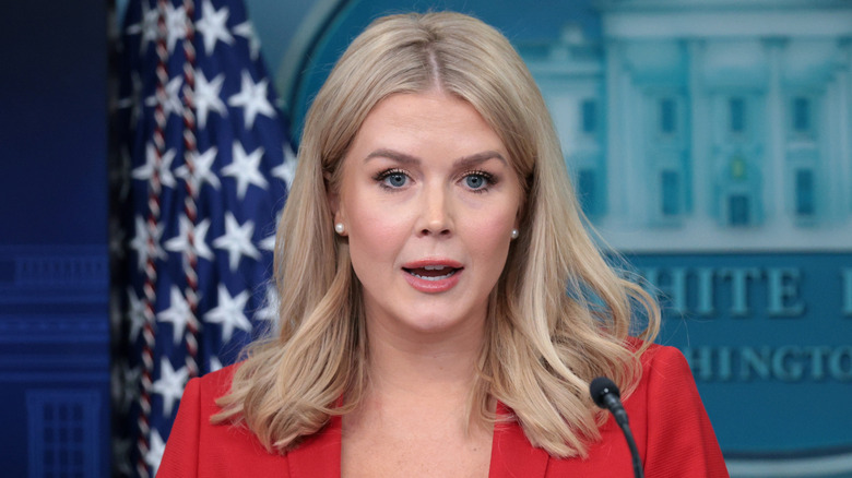 Karoline Leavitt speaking while wearing a red blazer at a press briefing.