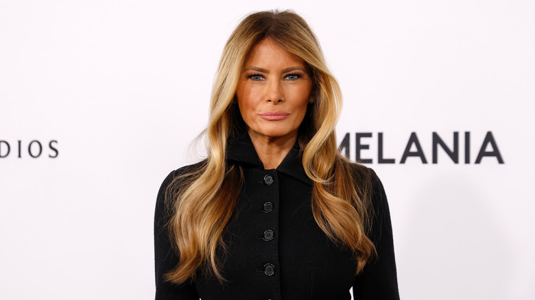 Melania Trump smirks while wearing a black cardigan