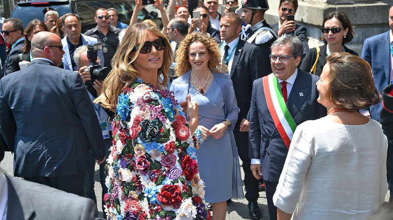 Melania Trump smiles while wearing a vibrant embroidered jacket covered in silk flowers