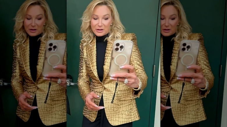 Paula White-Cain poses in a gold leather blazer while holding an iPhone