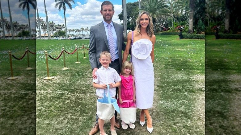 Lara Trump poses with her husband and young children in a white dress with a large flower detail on the front
