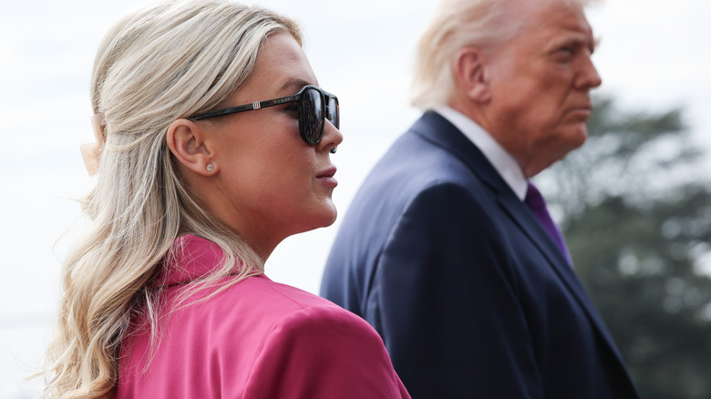 Karoline Leavitt sunglasses pink jacket with Trump background