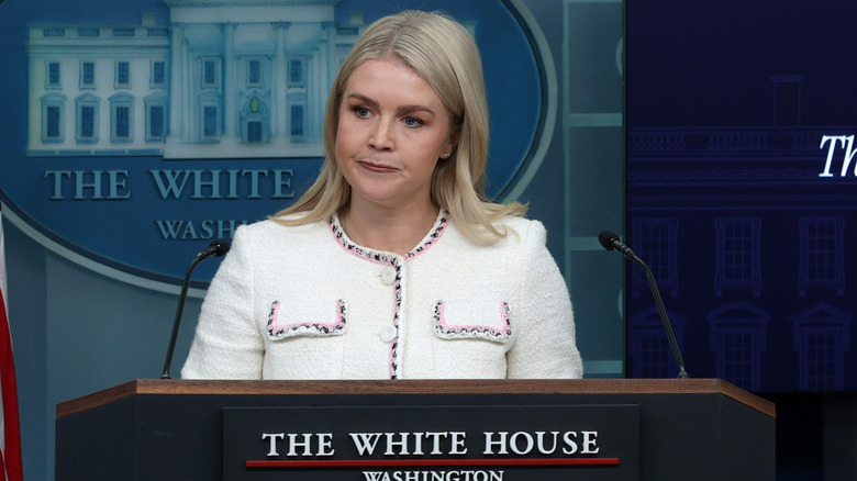 Karoline Leavitt pursing her lips at the podium in a white blazer