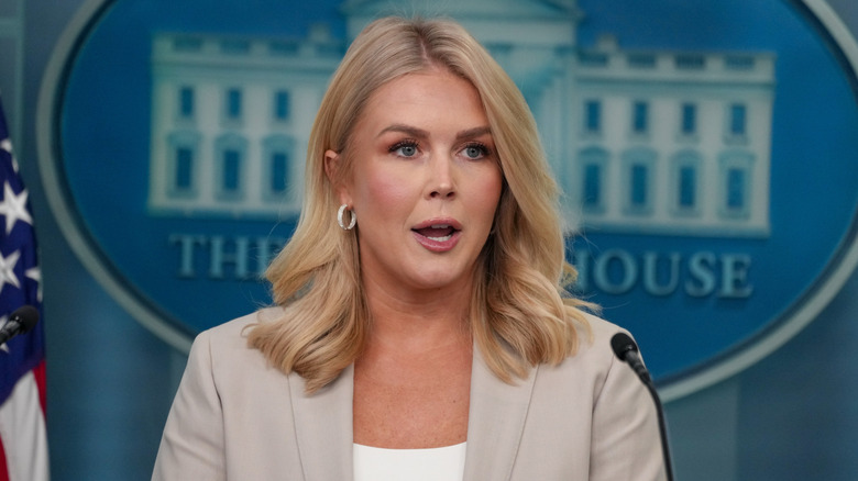 Karoline Leavitt at White House podium wearing a tan jacket