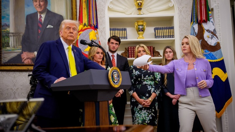 Karoline Leavitt hands Donald Trump a document